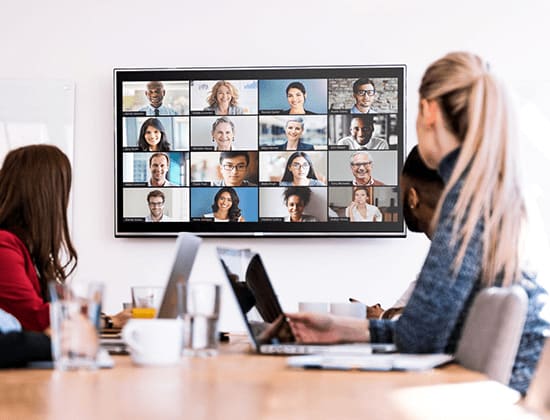 Personal en una sala de reuniones mirando un Display con una videoconferencia en curso